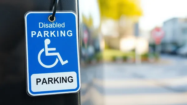 Placa azul de vaga de estacionamento reservada para pessoa com deficiência em frente a um carro com cartão visível no painel